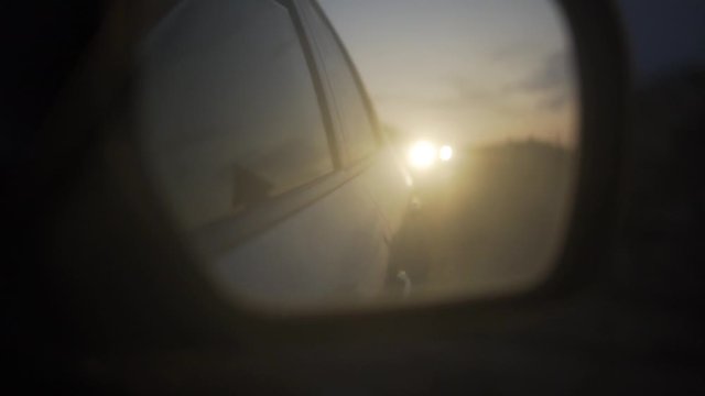 close up of a car mirror reflection on the road  at sunset,  car lights behind , b roll