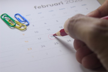 Simple Top View Close Up Photo Illustration, Re-Schedule Marked by man Hand with Red Color Pencil, Focus to Date at calendar

