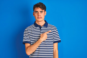 Teenager boy wearing casual t-shirt standing over blue isolated background Pointing aside worried...