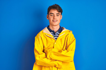 Teenager fisherman boy wearing yellow raincoat over isolated background happy face smiling with crossed arms looking at the camera. Positive person.
