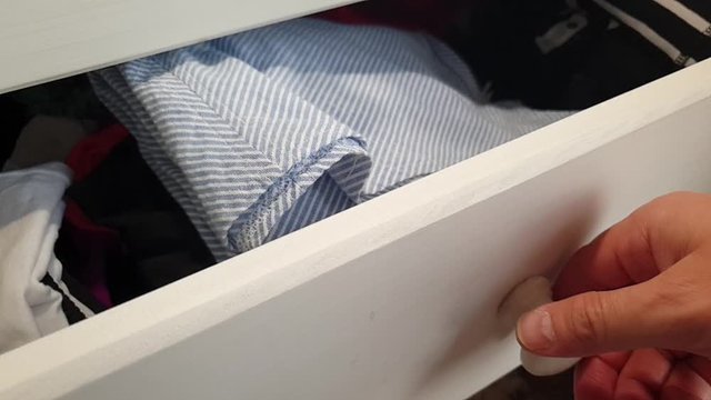 White wooden clothing dresser with neatly folded and washed shirts, underwear and dresses being opened or closed by hand in house bedroom