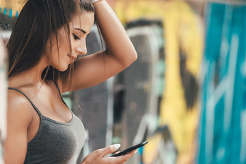 Closeup of female hipster with smart phone. Woman using smartphones against colorful graffiti wall