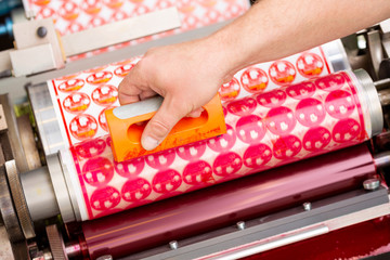 Process of removing possible dust debris on polymer plate in magenta print tower station with sticky roll on flexographic printing press. Dirt removing from photopolymer in flexo print machine.