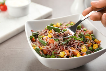 Woman eating tasty brown rice with vegetables at grey table, closeup