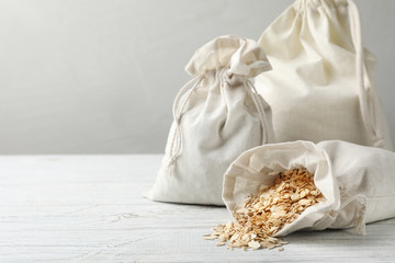Cotton eco bags with oat flakes on white wooden table. Space for text