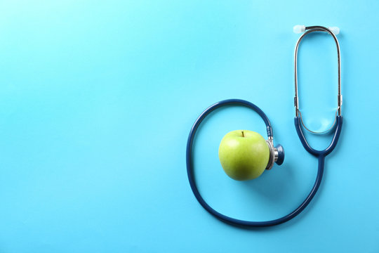 Flat lay composition with apple and stethoscope on light blue background. Space for text