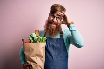 Redhead Irish supermarket worker man with beard wearing apron and holding fresh groceries stressed...