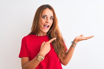 Young redhead woman wearing red casual t-shirt stading over white isolated background amazed and...