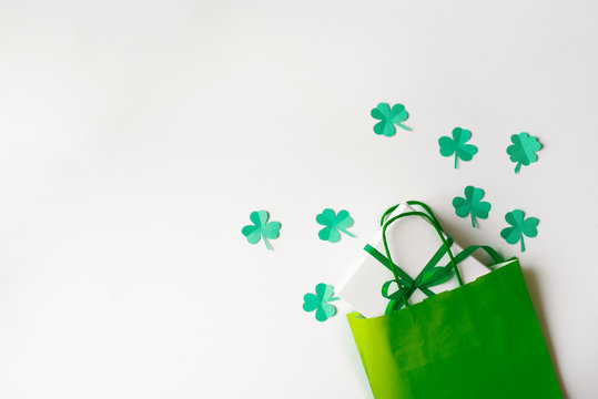 Discounts for St. Patrick's Day. Green paper bag and paper clover leaves, gift box with a green bow on a white background.