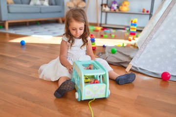Adorable blonde toddler playing with car toy around lots of toys at kindergarten