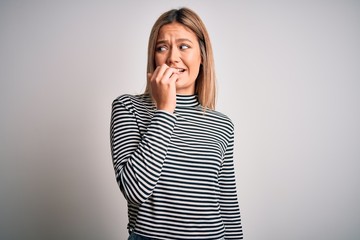 Young beautiful blonde woman wearing casual striped sweater over isolated background looking stressed and nervous with hands on mouth biting nails. Anxiety problem.