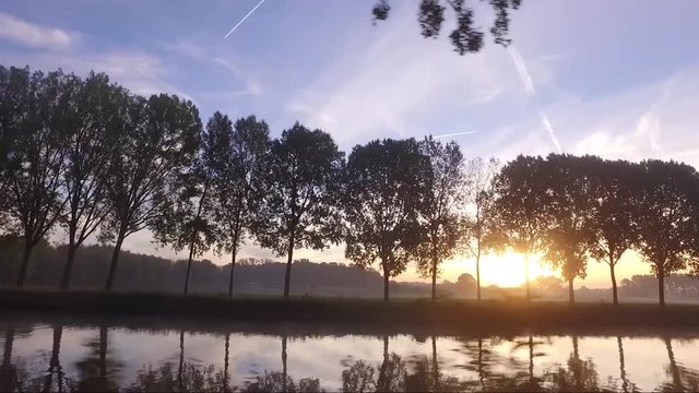 Sunrise on the schelde river with fog on the, water and the sun behind the threes, camera movement to the front with a bridge
