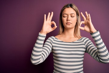 Fototapeta premium Young beautiful blonde woman wearing casual striped shirt over purple isolated background relax and smiling with eyes closed doing meditation gesture with fingers. Yoga concept.