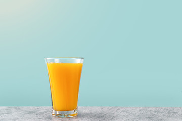 One glass of orange juice on light yellow background