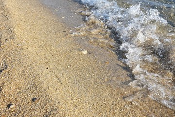 Transparent blue sea wave with white foam on a clean sandy shore, selective focus. turquoise ocean water with splashes. Summertime. Empty sand beach with beautiful pink wave background. Summer rest