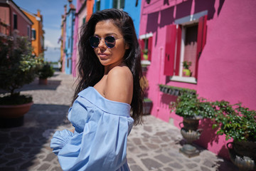  Young fashionable woman in romantic blue  dress  with braid hairstyle, posing near colorful houses in Burano Island, Venice, Italy