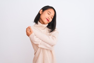 Young chinese woman wearing turtleneck sweater standing over isolated white background Hugging...