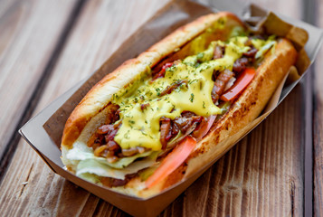 Philly cheese steak sandwich with meat, vegetables, cheese and sause in box on wooden table. street food