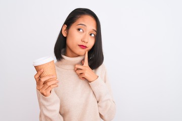 Young beautiful chinese woman drinking paper glass of coffee over isolated white background serious face thinking about question, very confused idea