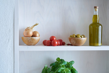 beautiful glass bottle of healthy organic cooking oil which can also be olive oil, on a white wall shelf in a Mediterranean style, surrounded by healthy vegetables such as olives, tomatoes and onions 