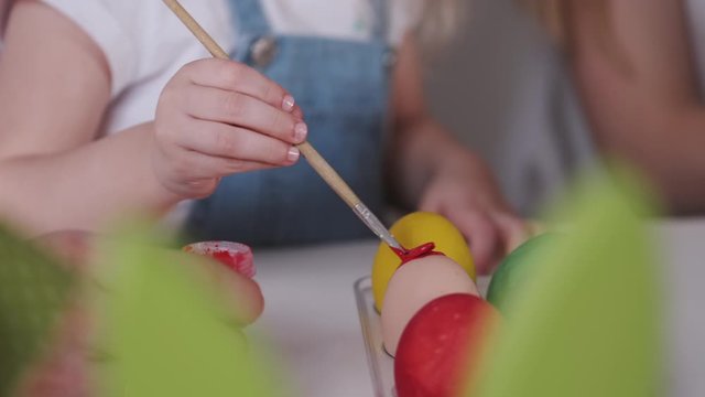 The easter eggs are being painted in different colors by hands. The family is preparing for the holiday.
