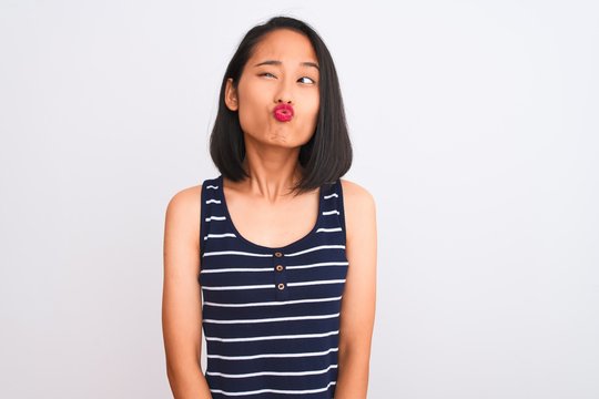 Young chinese woman wearing striped t-shirt standing over isolated white background making fish face with lips, crazy and comical gesture. Funny expression.