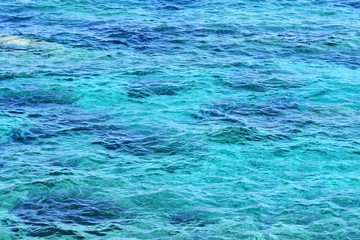 Soft focus. Abstract water background. Clean transparent azure water backdrop. Pure sea with sun glare on the surface of water. Textured water surface with selective focus and sun beams. Summertime 