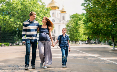 Obraz premium Happy family walking together. Pregnant mother, som and father spend time on city street.