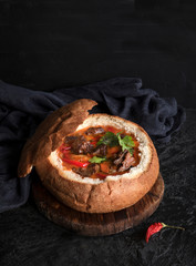 Goulash or thick soup is served in bread on a black background. Czech traditional cuisine. Copy...