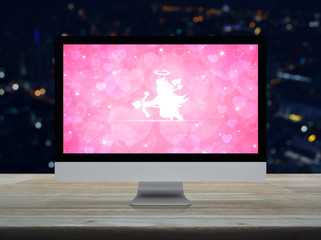 Cupid flat icon on desktop modern computer monitor with red love heart screen on wooden table over blur colorful night light city tower and skyscraper, Business internet dating online, Valentines day 