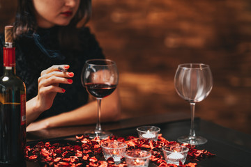 Alone and unhappy beautiful woman sitting on a table, drink wine and smoke with a bad mood.