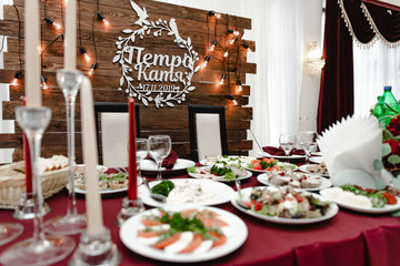 Decoration of wedding banquet. Table decorated by red flowers, greenery and candels. Wedding table with food