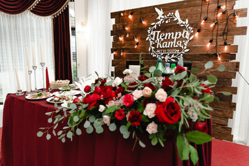 Decoration of wedding banquet. Table decorated by red flowers, greenery and candels. Wedding table with food