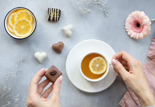 young  woman's hands with dark chocolate candy and a white cup of tea on a gray background. enjoy healthy lifestyle. horizontal image, top view, flat lay