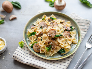 farfalle with mushrooms and spinach on a gray concrete background. Vegetarian pasta. horizontal image, close-up