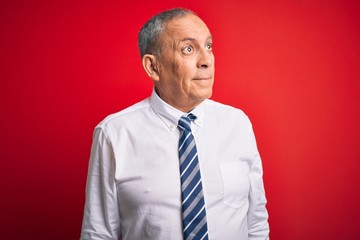 Senior handsome businessman wearing elegant tie standing over isolated red background smiling looking to the side and staring away thinking.