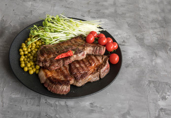 Juicy fried steak with a salad of sprouted peas, green peas and tomatoes on a gray concrete background. The concept of a healthy separate diet. Copy space