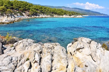 Seascape of rocky beach with blurred azure sea water in sunny day. Amazing natural beach with white stones and turquoise water. crystal clear sea with sun reflection. Halkidiki Greece Blue Flag Beach