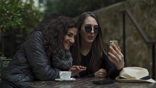 Two attractive young women sitting in cafe skyping with their family. facetime. 4K