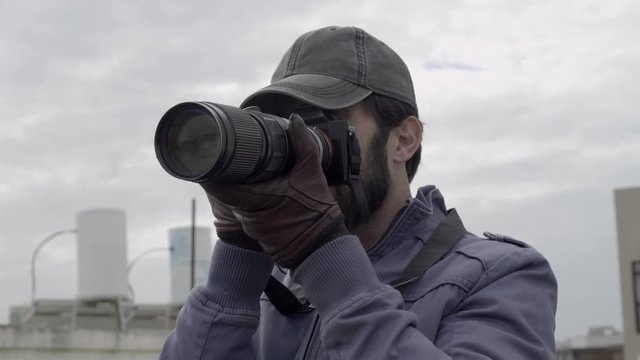 Serious private detective spying on suspects and shooting photos outside with his paparazzi camera. 4K