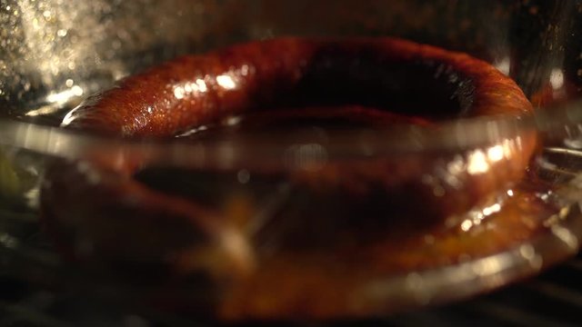 Juicy sausage cooking in transparent heatproof glass tray in oven, RACK FOCUS.
