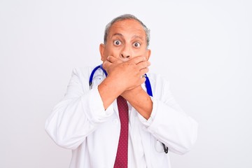 Senior grey-haired doctor man wearing stethoscope standing over isolated white background shocked covering mouth with hands for mistake. Secret concept.