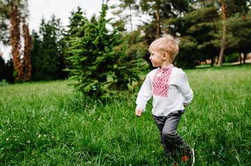 Happy little baby boy running in embroidered shirt on the background of nature. full length. looking sideways. Close up. Catch inflatable bubbles.