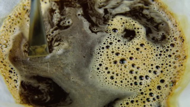 Slow motion stiring coffee with a silver spoon within a coffee filter