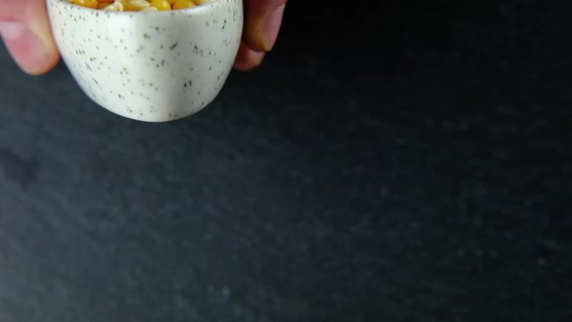 Slow motion pop corn popping kernels been poured in front of a black slate background left of the frame