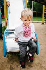 Boy going drive down on children's slide on the playground for children, outdoors. In an embroidered shirt. Close up. full length, looking down.