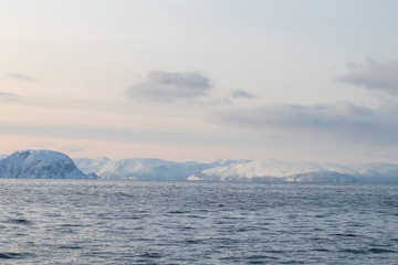 Arctic landscape in winter with snowy mountains and sea. Norwegian coasts and fjords seen from the boat in the open sea. Arctic polar north europe landscape with white snow and ice