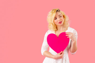 Studio portrait of a beautiful young woman holding pink heart and looking to side, romantic love, dating and Valentine's Day concept
