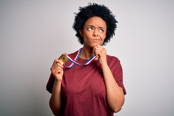 Young African American athlete woman with curly hair wearing gold medal winner competition serious face thinking about question, very confused idea