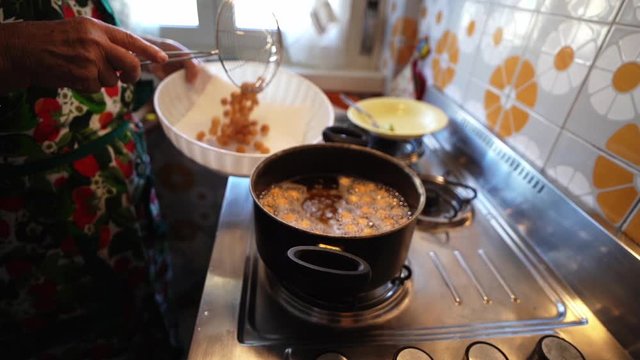 Drain boiling oil from fried struffoli pastries to put in bowl